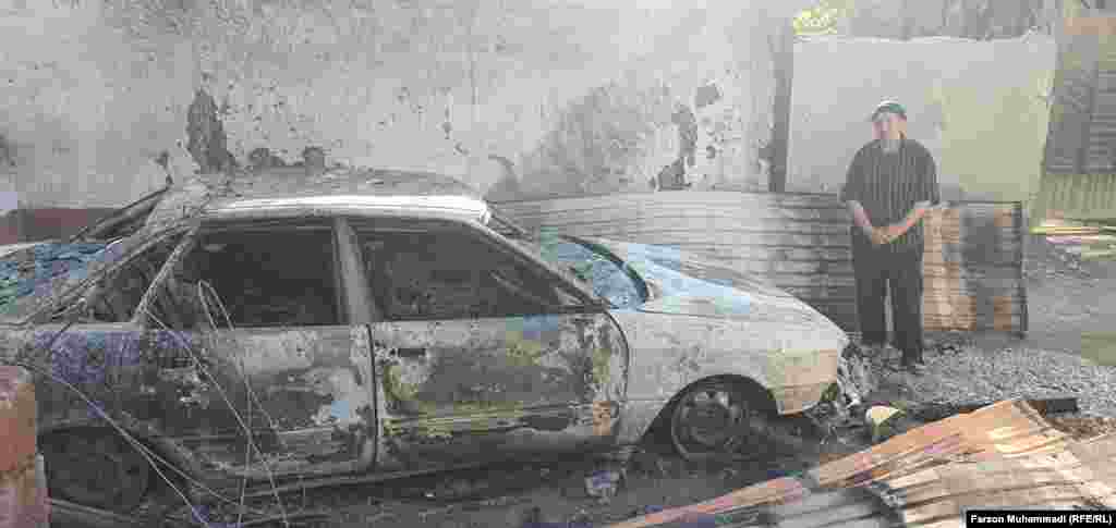 A local resident stands behind a burned car in Somoniyon, Tajikistan.