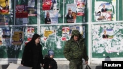 People pass by campaign posters in Tskhinvali displaying presidential candidates in South Ossetia's March 25 repeat election.