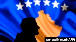 A man stands in front of a screen displaying the Kosovo flag in Pristina.