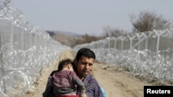 A migrant from Afghanistan holding a child walks next to a border fence at the Macedonian-Greek border in Gevgelija.