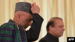 Visiting Afghan President Hamid Karzai (left) is flanked by Pakistani Prime Minister Nawaz Sharif as he adjusts his cap in Islamabad on August 26.