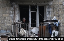 A woman looks out the window of a damaged apartment building in Stepanakert.